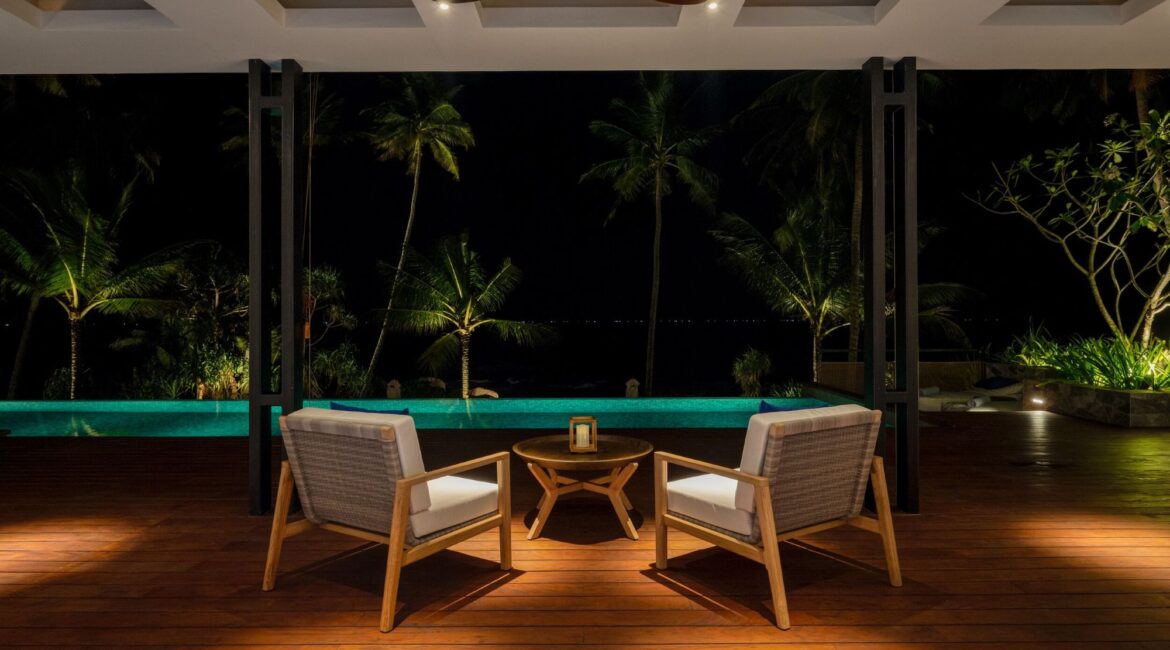 Swimming pool at Ahu Bay Sri Lanka illuminated at night, reflecting palm trees and the ocean beyond.