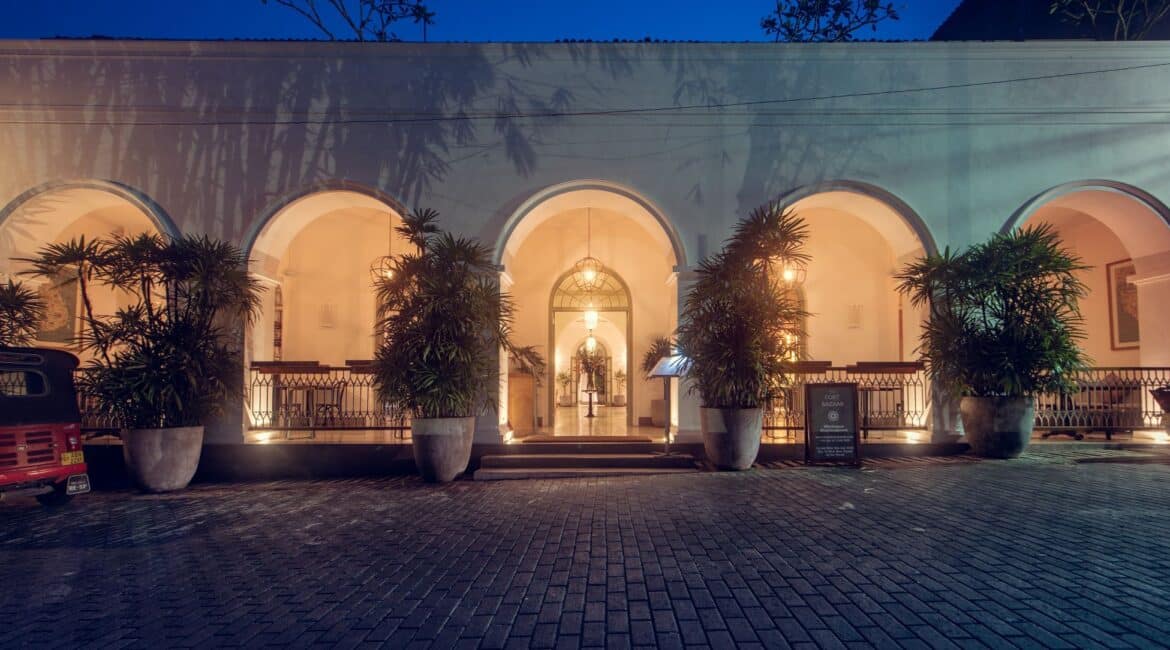 Entrance of Fort Bazaar Hotel Sri Lanka by night, warmly illuminated with lanterns highlighting the arched doorway and colonial-style architecture.