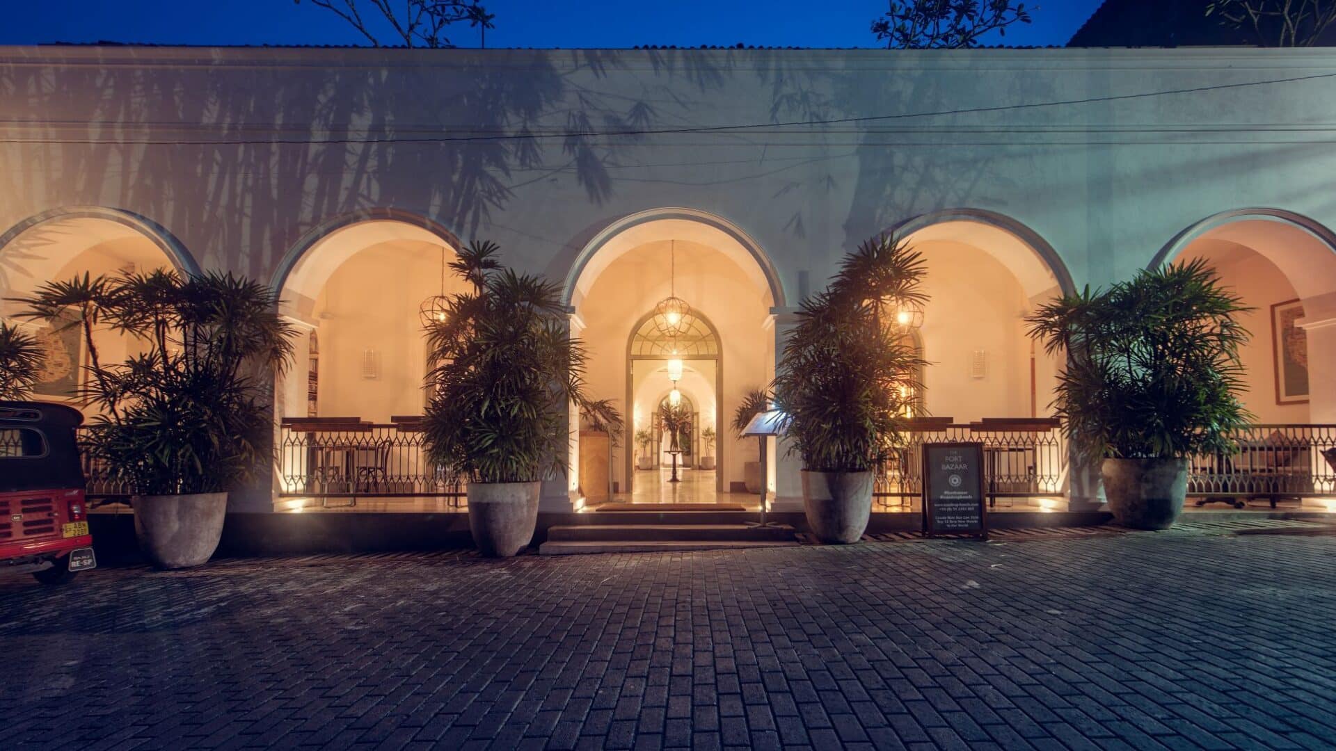 Entrance of Fort Bazaar Hotel Sri Lanka by night, warmly illuminated with lanterns highlighting the arched doorway and colonial-style architecture.