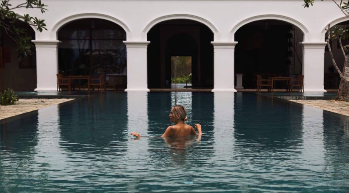 Kayaam House Sri Lanka – guest swimming in the tranquil infinity pool with the elegant hotel building framed in the background.
