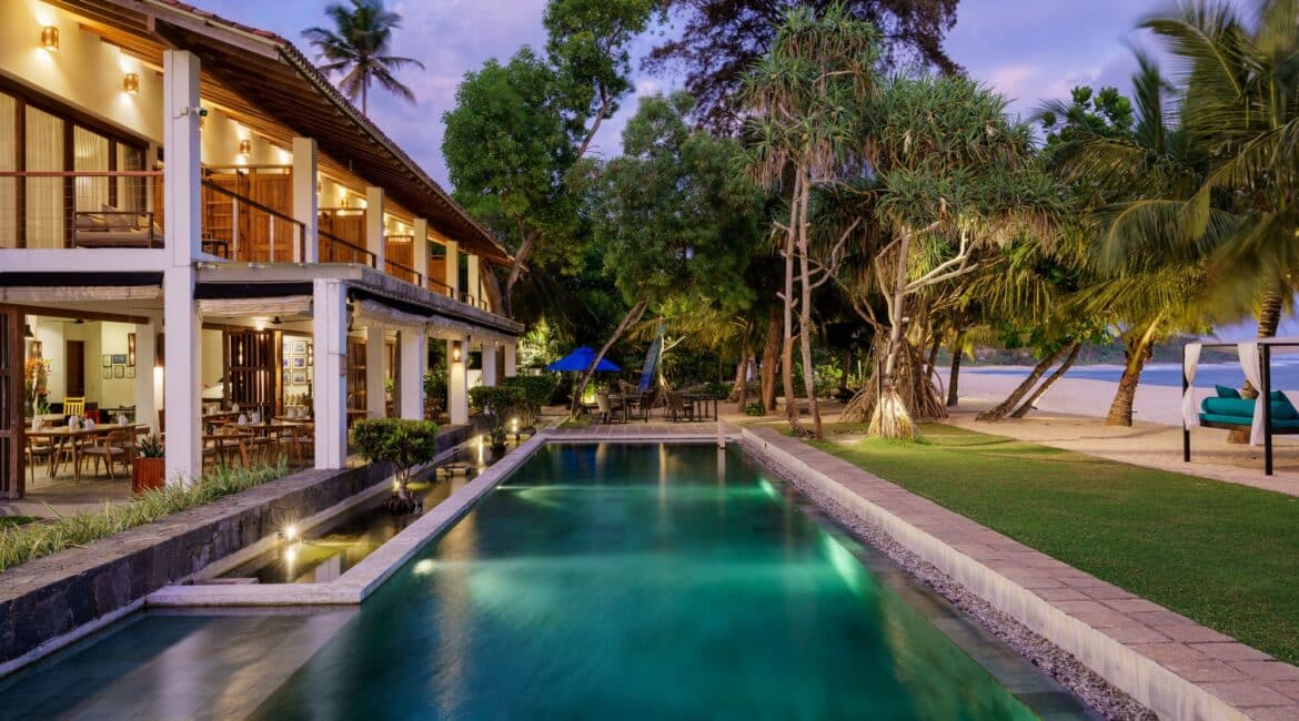 Lantern Boutique Hotel Sri Lanka – early evening view of the illuminated swimming pool, beachfront grounds, and glowing hotel exteriors with the Indian Ocean beyond
