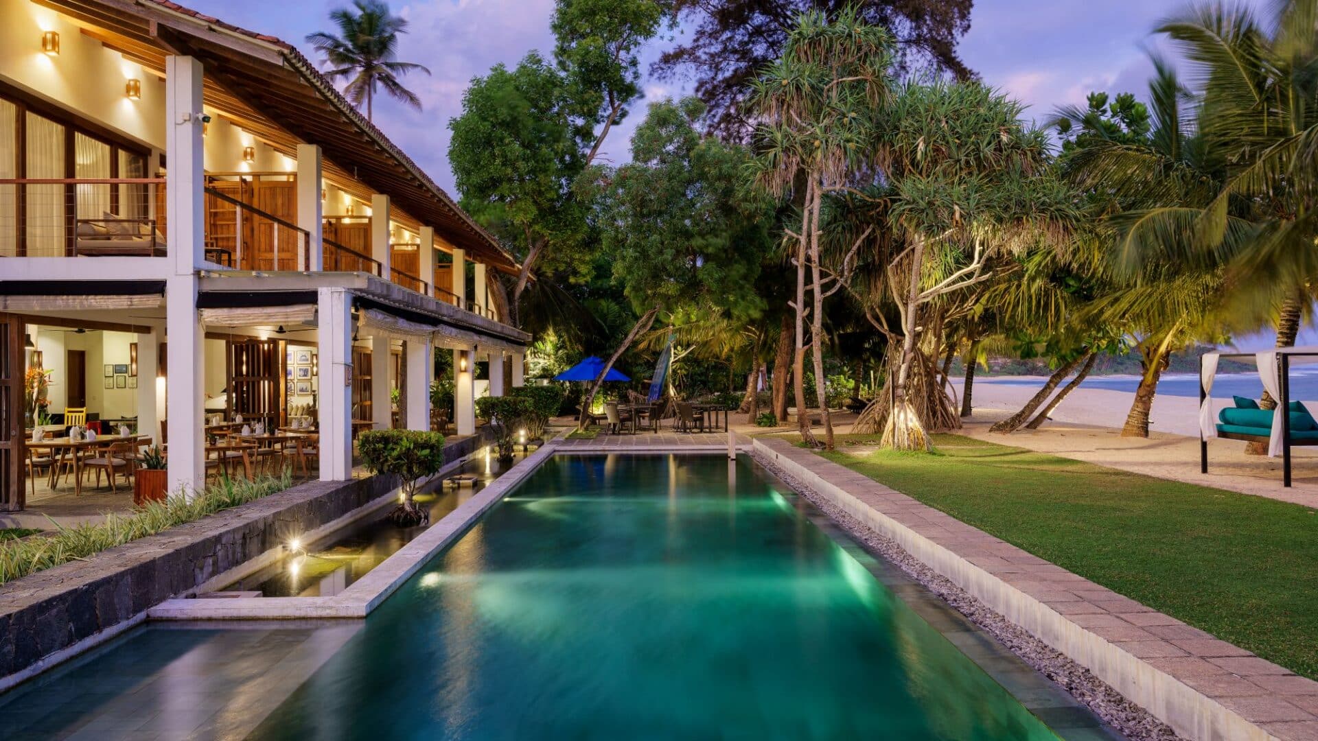 Lantern Boutique Hotel Sri Lanka – early evening view of the illuminated swimming pool, beachfront grounds, and glowing hotel exteriors with the Indian Ocean beyond