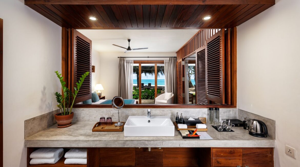 Ocean Suite at Lantern Boutique Hotel Sri Lanka – en suite bathroom with open shutters framing views through the bedroom to the balcony, Indian Ocean, and beach beyond