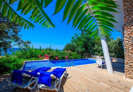 Sea-facing terrace at Likya Pavilion Pool House in Kalkan with daybeds, large private pool, blue skies, and stone façade backdrop